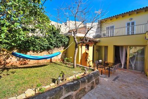 A yellow building with a balcony, a hammock, and a patio area with a table and chairs.