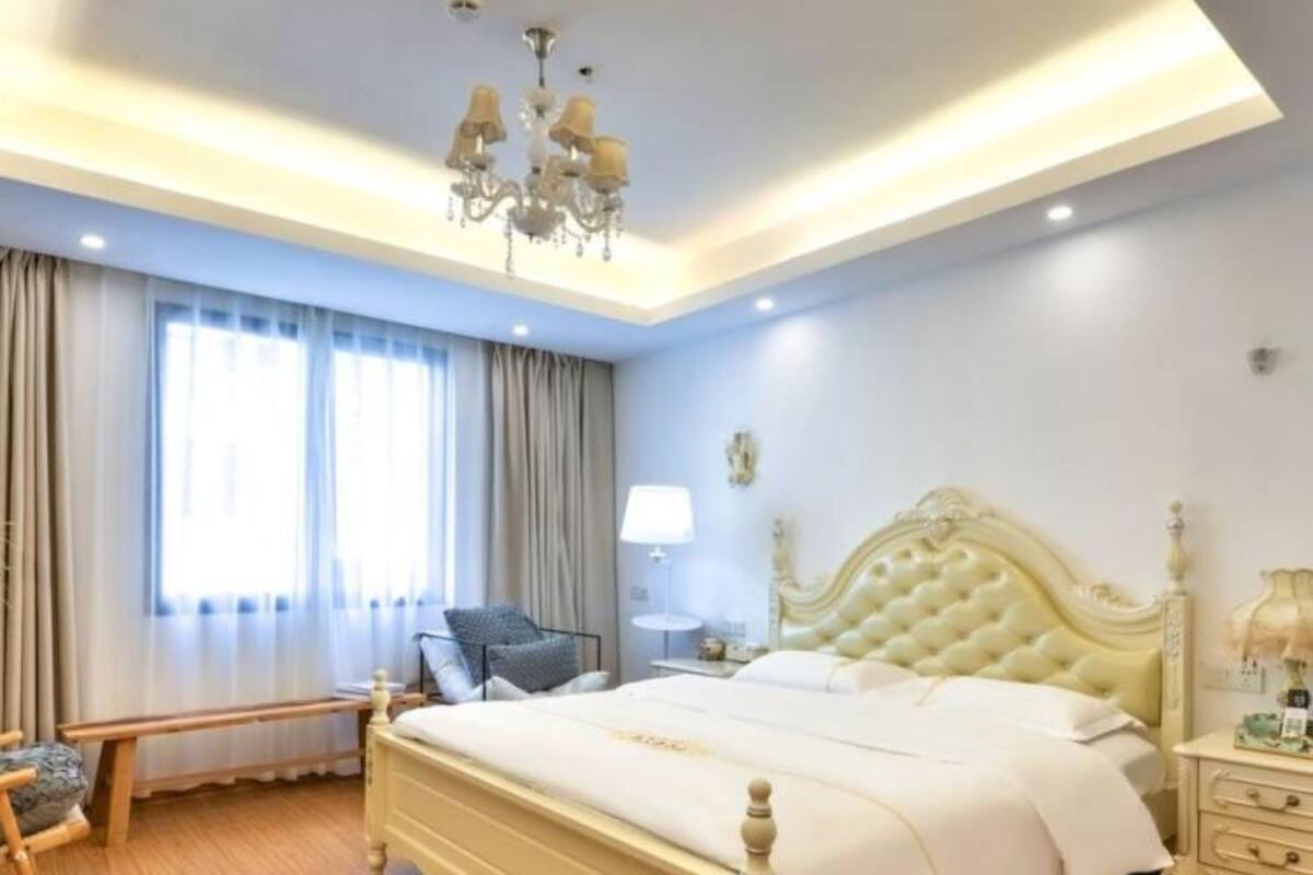 A bedroom with a large bed, a chandelier, a bedside table, and a window with curtains.