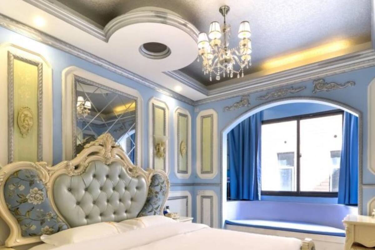 A bedroom with a large bed, ornate headboard, and a chandelier.