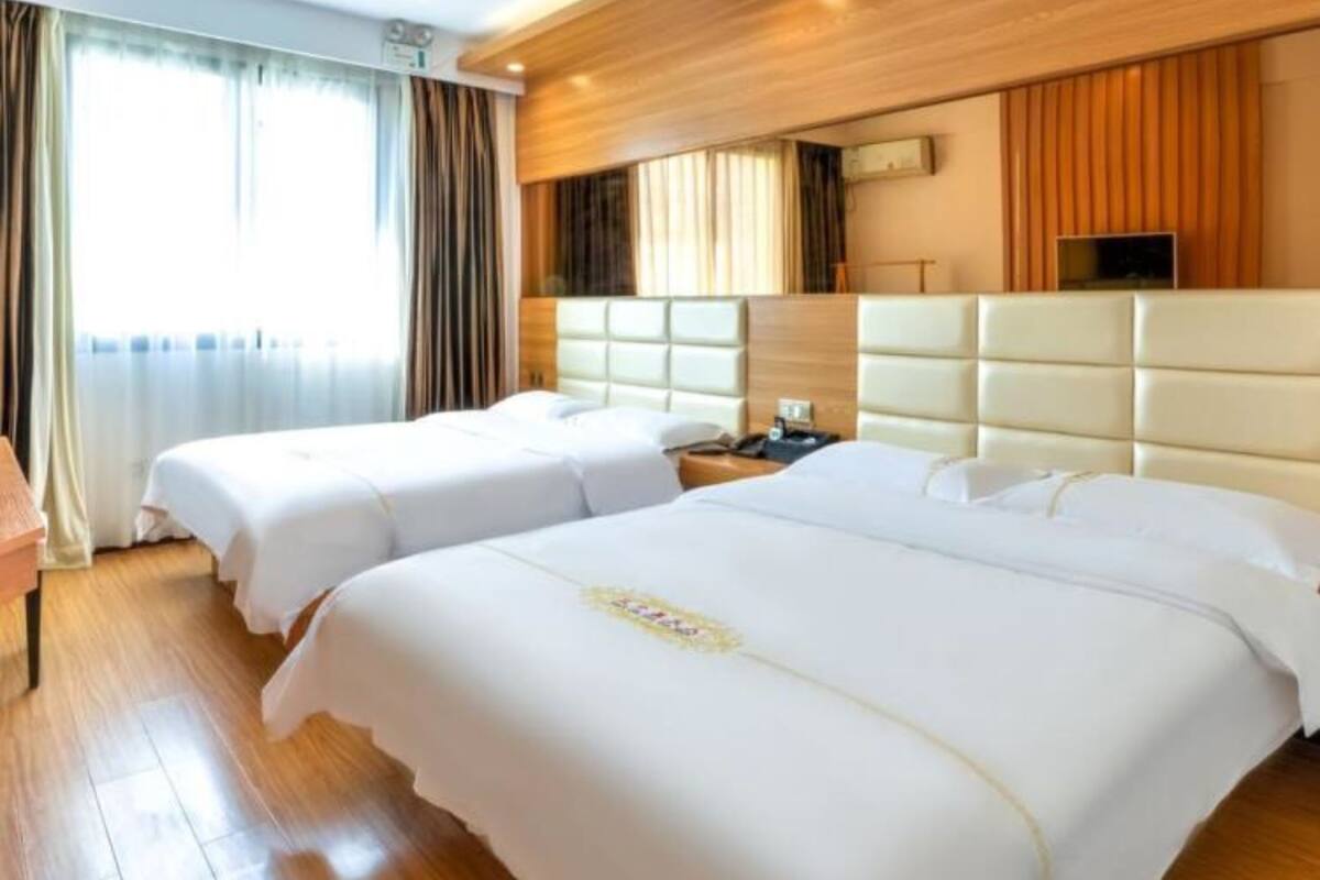 A hotel room with two beds, wooden paneling on the walls, a large window with curtains, and a flat-screen TV mounted above the beds.