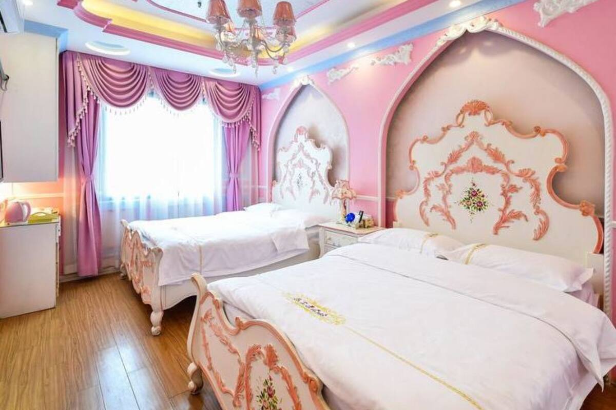 A bedroom with two beds, a chandelier, and pink and white decor.