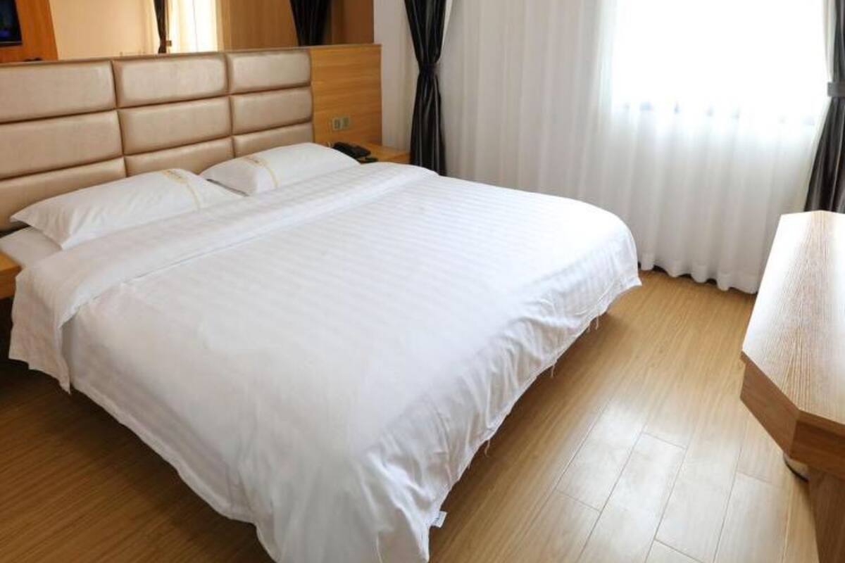 A hotel room with a large bed, wooden headboard, and a nightstand with a lamp.