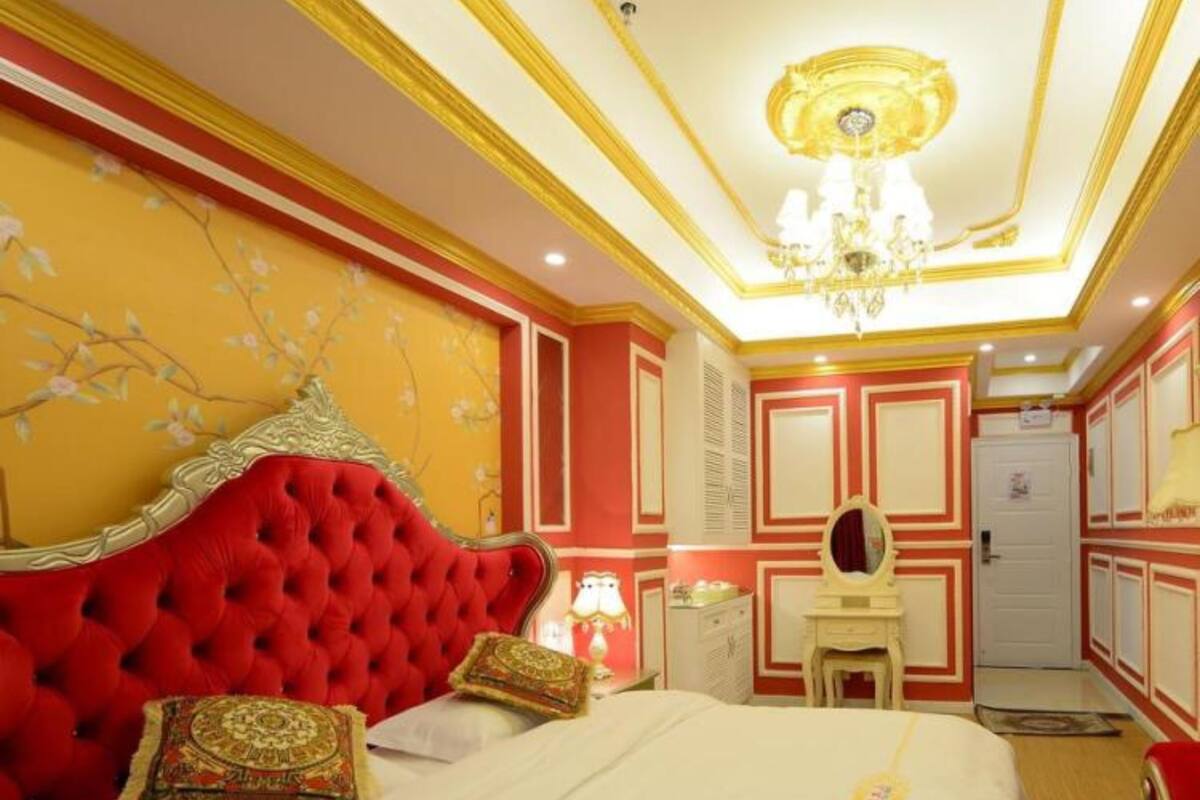 A bedroom with a red tufted headboard, a white bedspread, and a chandelier.