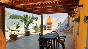 Une terrasse couverte avec un plafond en bois, une table avec des chaises, des plantes en pot et un barbecue.