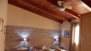 Une chambre avec un plafond en bois, un mur en briques, un lit recouvert d’une courtepointe, deux lampes de chevet et une table de chevet.