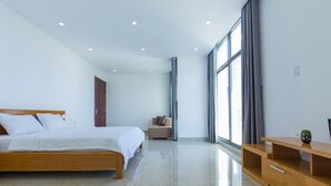 A modern bedroom with a wooden bed, a small seating area, and a large window providing natural light. - Villa Royal 2 (Ho Chi Minh City)