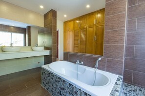 A modern bathroom with a freestanding bathtub, a vanity with two sinks, and wooden cabinets. - Villa Royal 2 (Ho Chi Minh City)