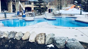 Un área de piscina con sillones de descanso, un jacuzzi y un tobogán cubierto de nieve.