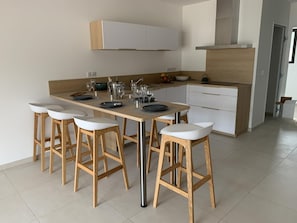 A modern kitchen with a central island, bar stools, and white cabinetry. - Hotel Calarossa Bay Resort (Lecci)