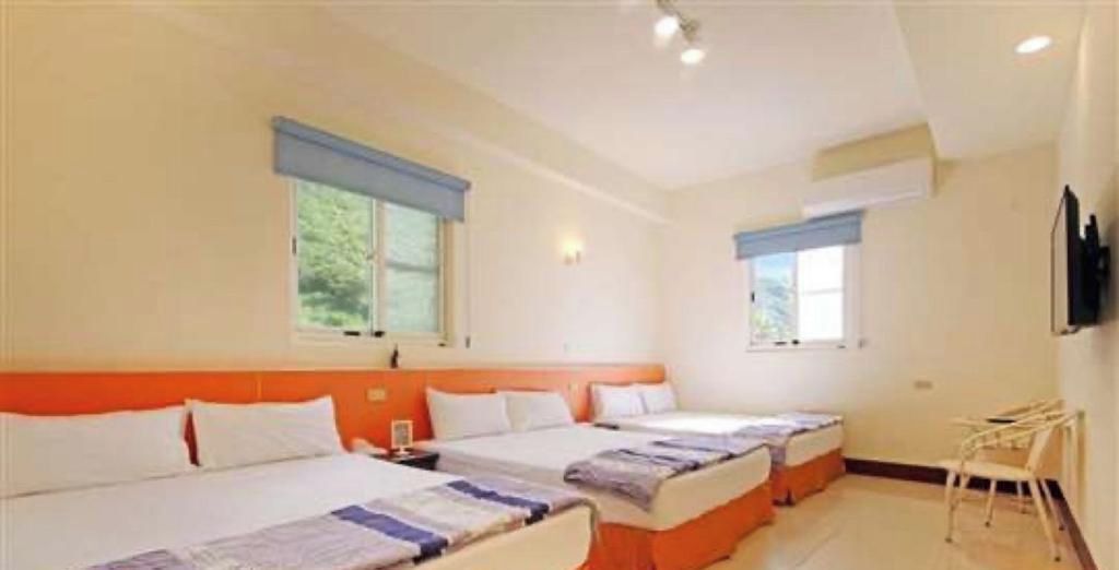 Une chambre d’hôtel avec deux lits, une chaise et un téléviseur fixé au mur.