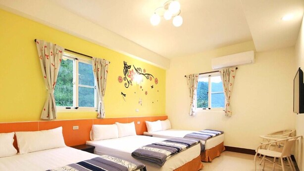 Ein Hotelzimmer mit drei Betten, zwei mit Vorhängen versehenen Fenstern, einem kleinen Tisch und einem Stuhl.
