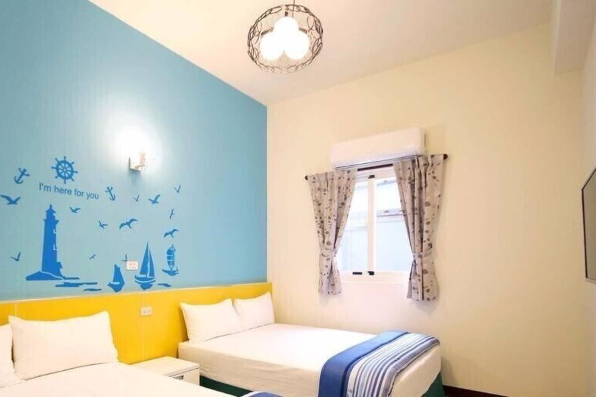 Habitación de hotel con cama, ventana con cortinas, pared decorada con motivos náuticos y una lámpara en el techo.