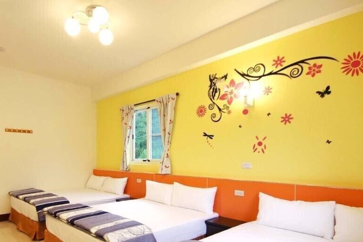 Habitación de hotel con tres camas, una ventana con cortinas y una pared decorada con motivos florales y mariposas.