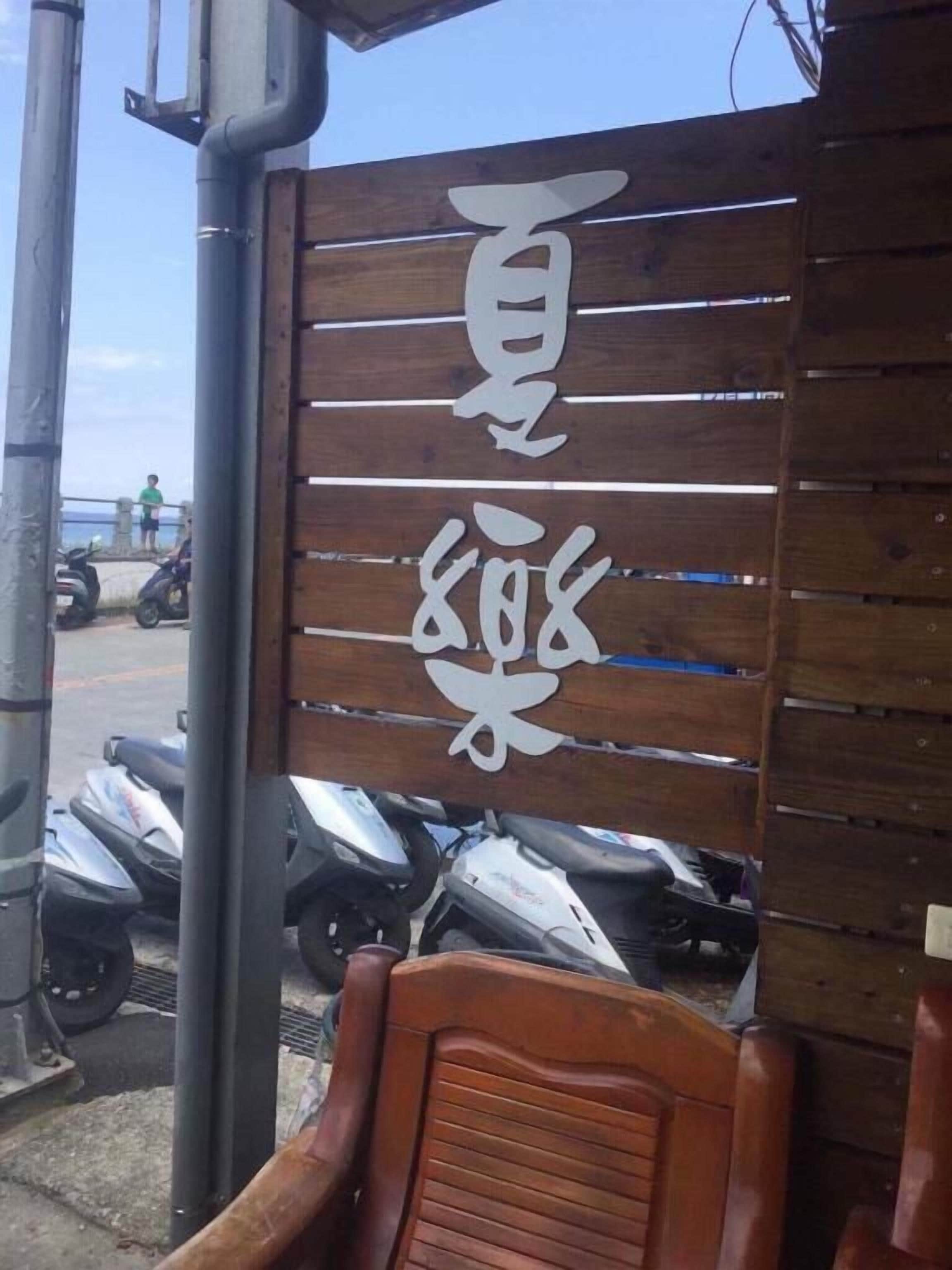Un letrero de madera con caracteres blancos, una moto estacionada al frente y una silla en primer plano.