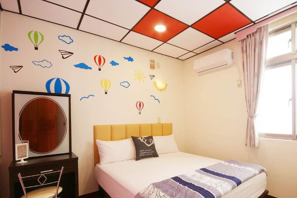 Habitación de hotel con cama, mesita de noche, una silla, ventana con cortinas y pared decorada con pegatinas con motivos meteorológicos.
