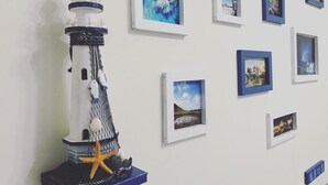 Ein Modellleuchtturm mit Seestern und Seil auf einem Sockel, umgeben von gerahmten Bildern an einer Wand.
