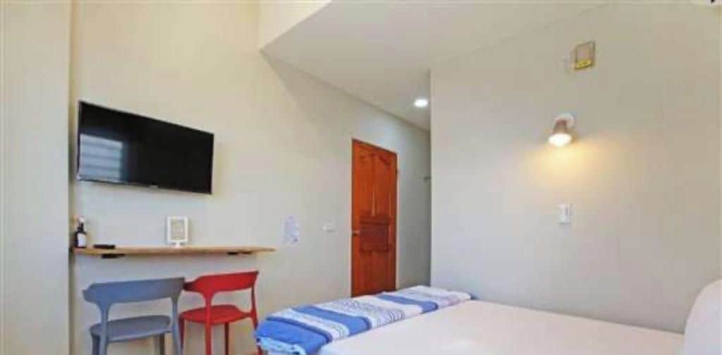 Una habitación pequeña con una cama, un escritorio, dos sillas, un televisor y una puerta.