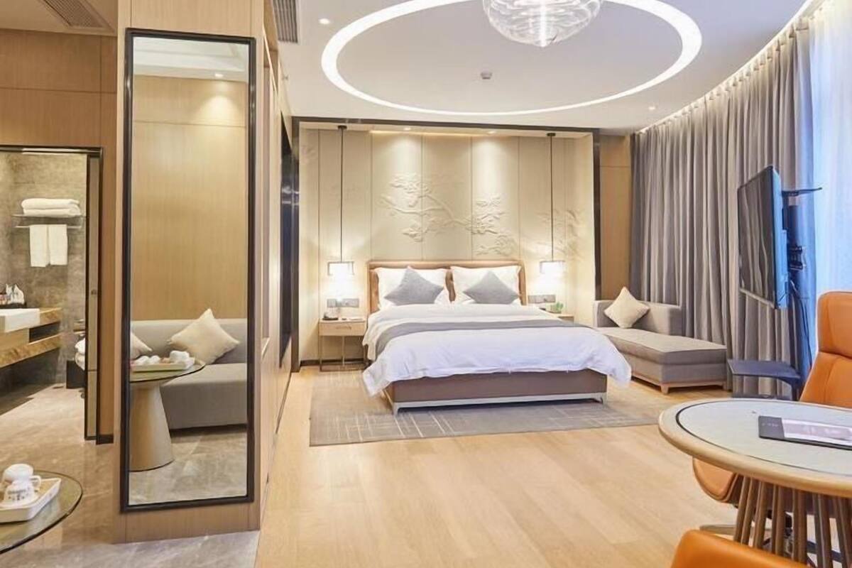 A modern hotel room with a large bed, a sitting area with a round table, and a TV.