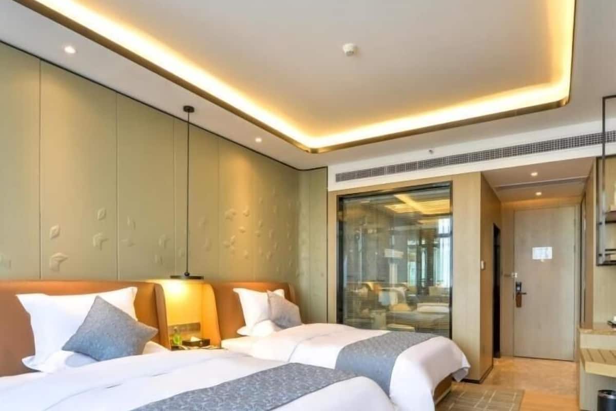 A modern hotel room with two beds, a large window, and a view of the city.