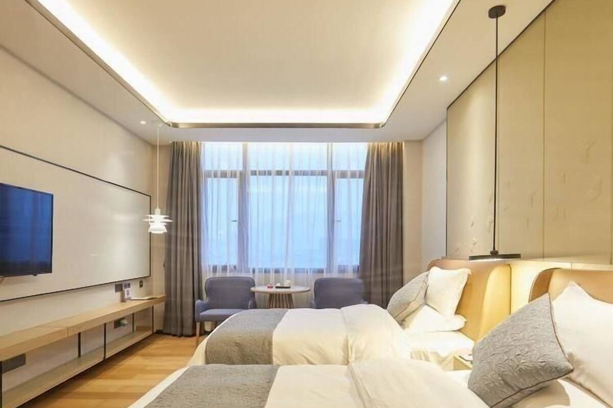 A hotel room with two beds, a TV, a desk, and a window with curtains.