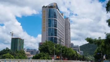 A modern high-rise building with a curved facade, surrounded by greenery and a clear sky.