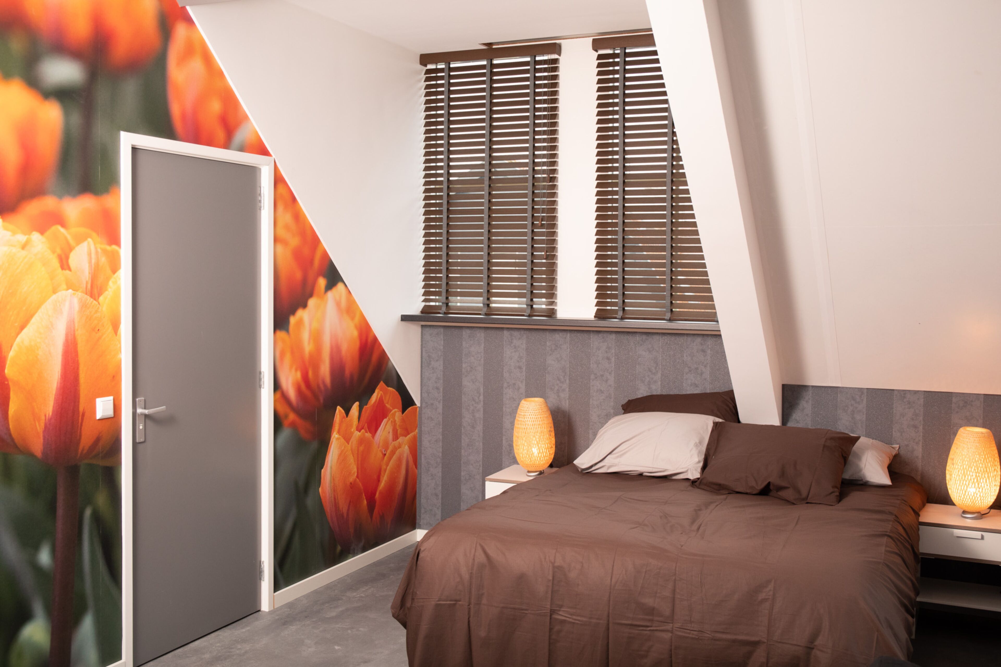 Un dormitorio moderno con cama, mesitas de noche, lámpara de pared y una puerta.
