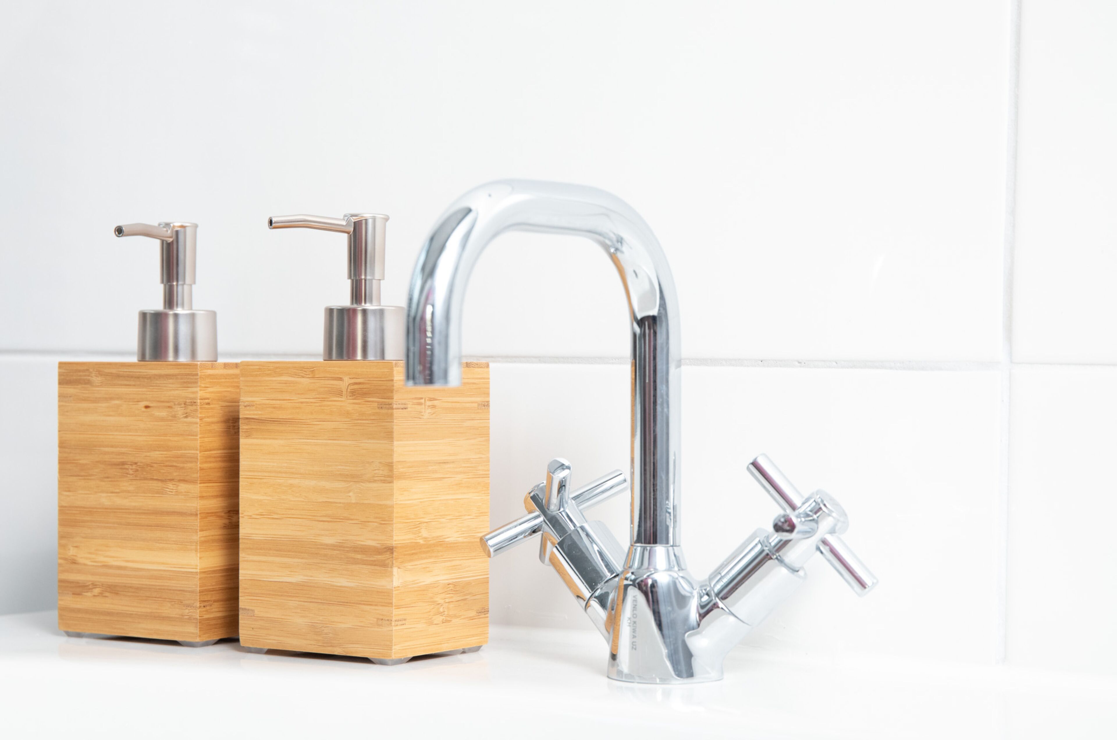 A modern bathroom with a chrome faucet, wooden soap dispensers, and a white tiled wall.