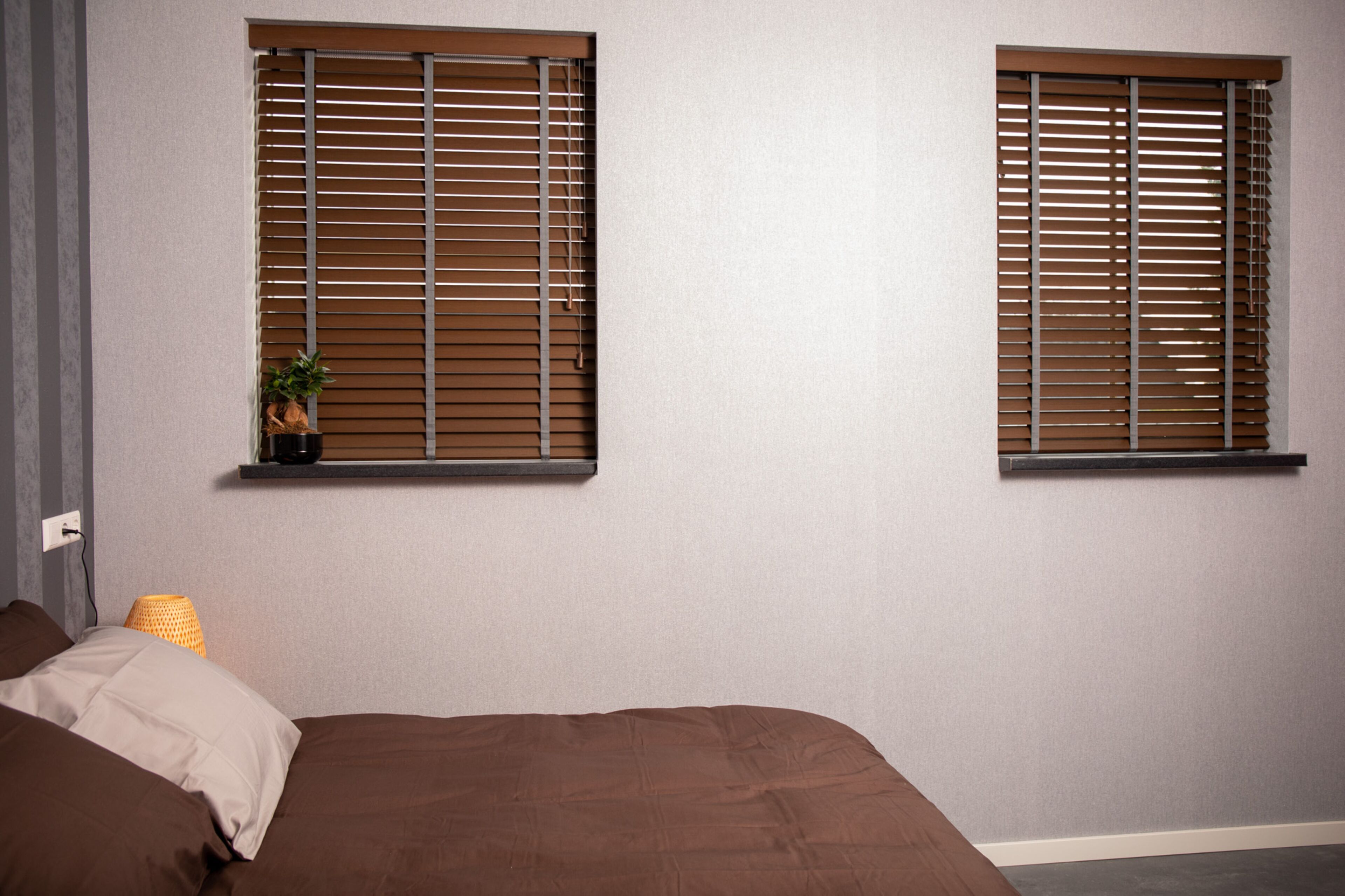 A bedroom with two windows, a bed, a nightstand, and a lamp.