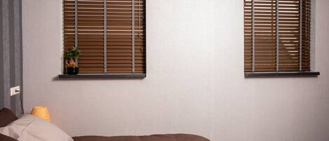 A bedroom with two windows, a bed, a nightstand, and a lamp.
