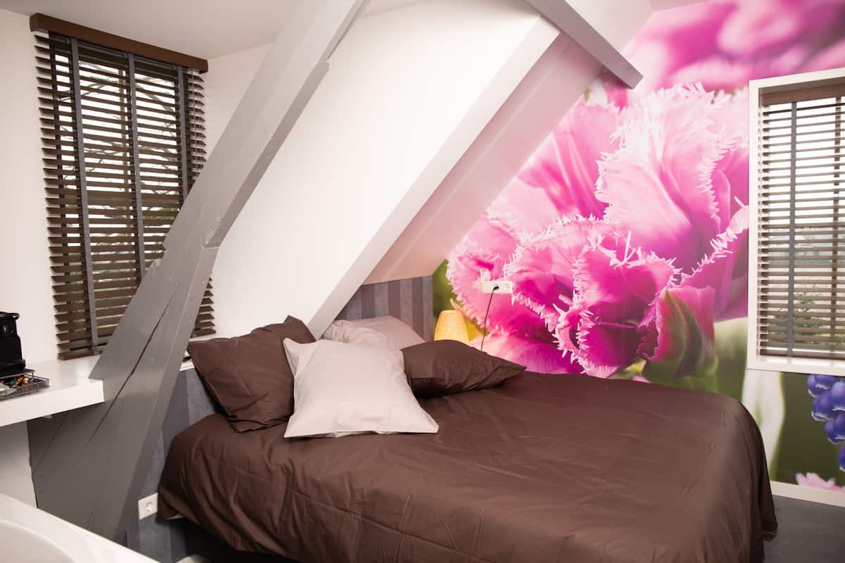 A bedroom with a sloped ceiling, a bed with brown bedding, and a large floral mural on the wall.