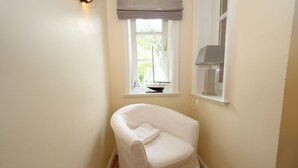 A corner room with a white chair, a window with a sailboat model, and a lamp.