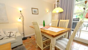 A dining area with a wooden table, four chairs, a floor lamp, and a sofa with a cushion featuring an anchor design.