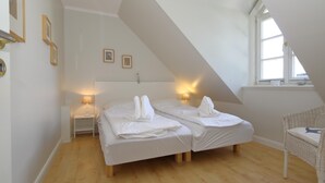A bedroom with two beds, a small table, a chair, and a window.