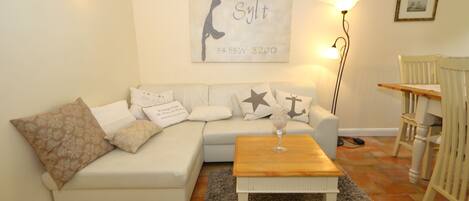 A living room with a white sofa, a wooden coffee table, and a rug. There is a wall-mounted artwork with the text "Slyt 5455'N 8200".