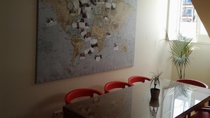 Zona pranzo con una grande mappa del mondo appesa al muro, un tavolo in vetro e sedie rosse.