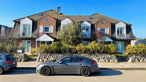 Une rangée de maisons de ville en briques, avec un garage central, des murs en pierre et une voiture argentée garée devant.