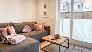 Un salon avec un canapé gris, une table basse en bois et une porte-fenêtre coulissante donnant sur un balcon.