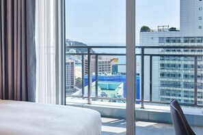 A hotel room with a large window offering a view of a cityscape, including buildings and a body of water. - Lavi de Atlan Hotel (Busan)
