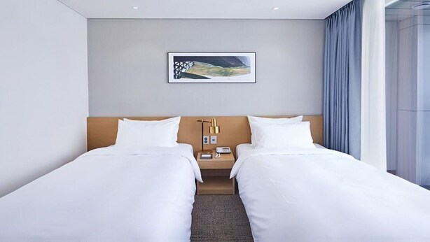 A hotel room with two single beds, a nightstand with a lamp, a phone, and a framed picture on the wall. - Lavi de Atlan Hotel (Busan)