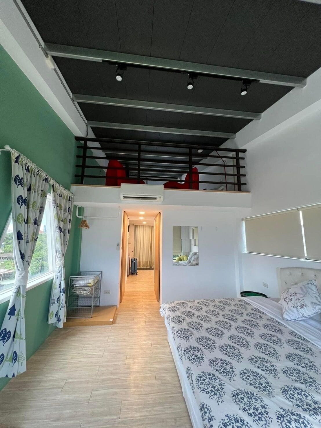 A two-story room with a bed, a small kitchenette, and a balcony with red chairs.