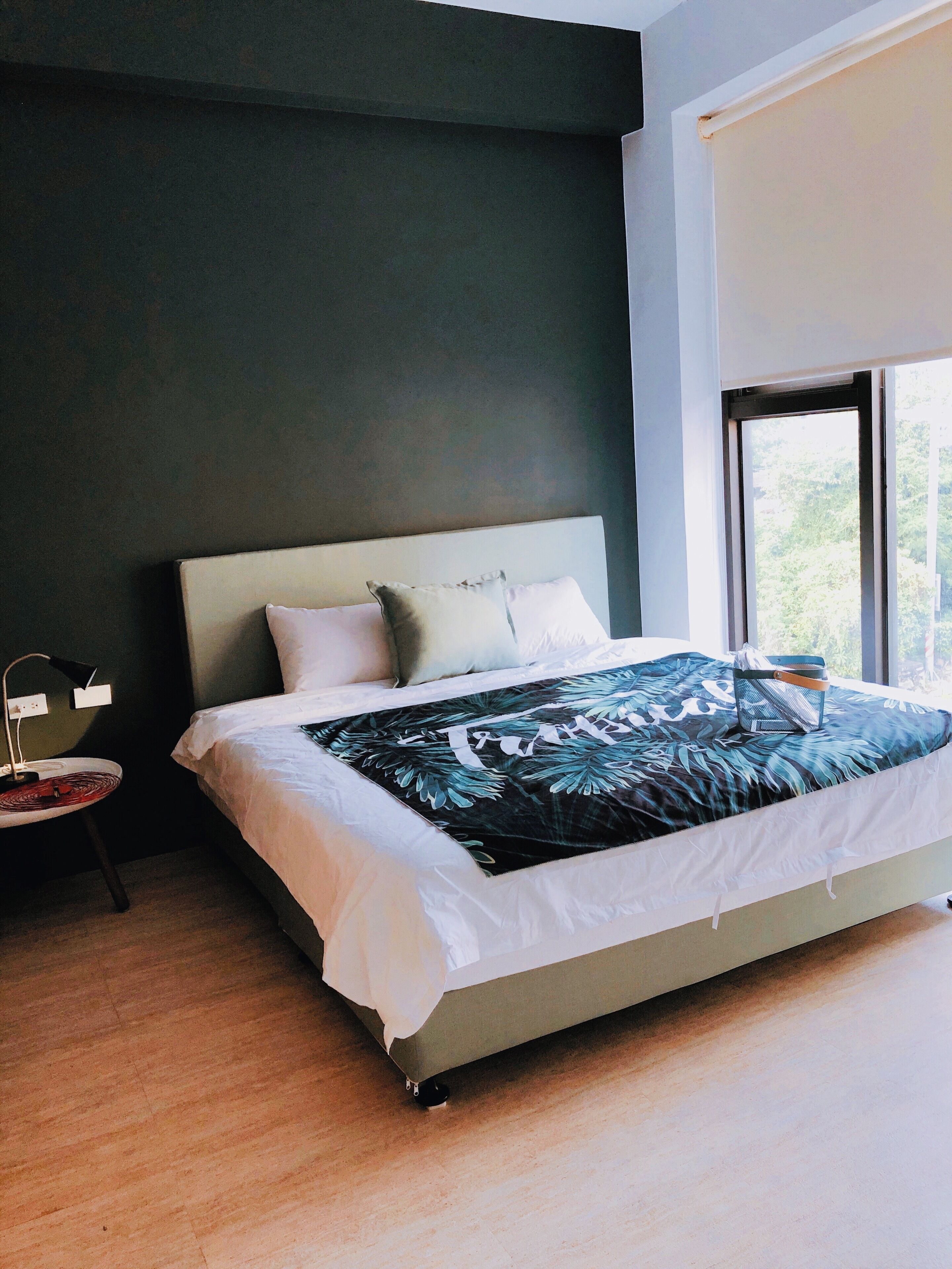 Un dormitorio moderno con una cama grande, una mesita de noche con lámpara y una ventana que da a zonas verdes.