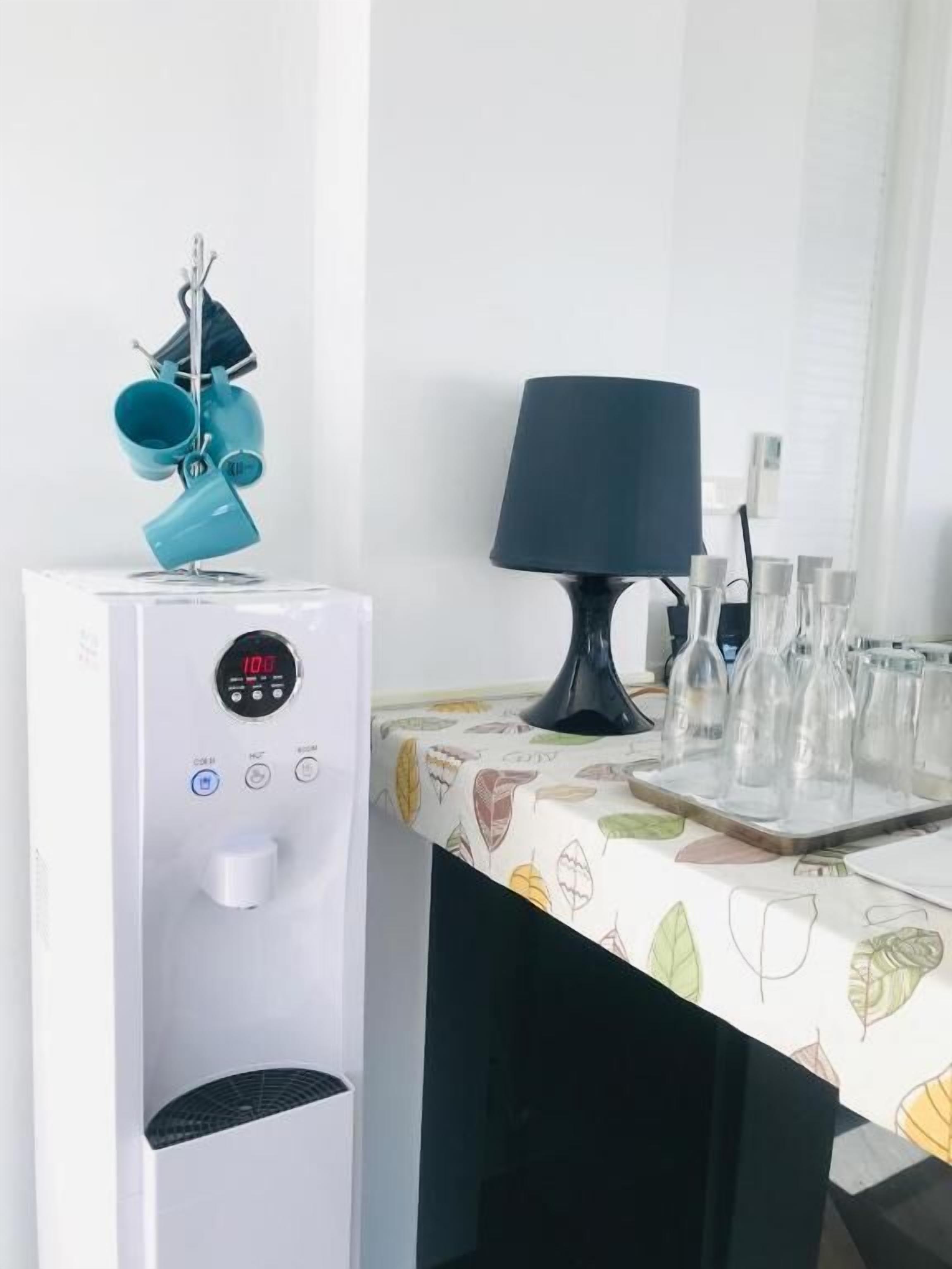 A room with a white water dispenser, a table with a leaf-patterned tablecloth, and a black lamp.