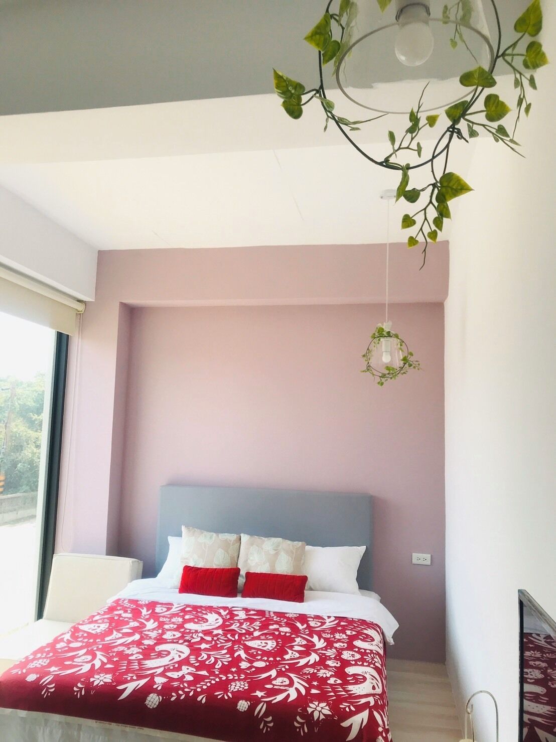 A bedroom with a bed, a window, and a wall-mounted light fixture.