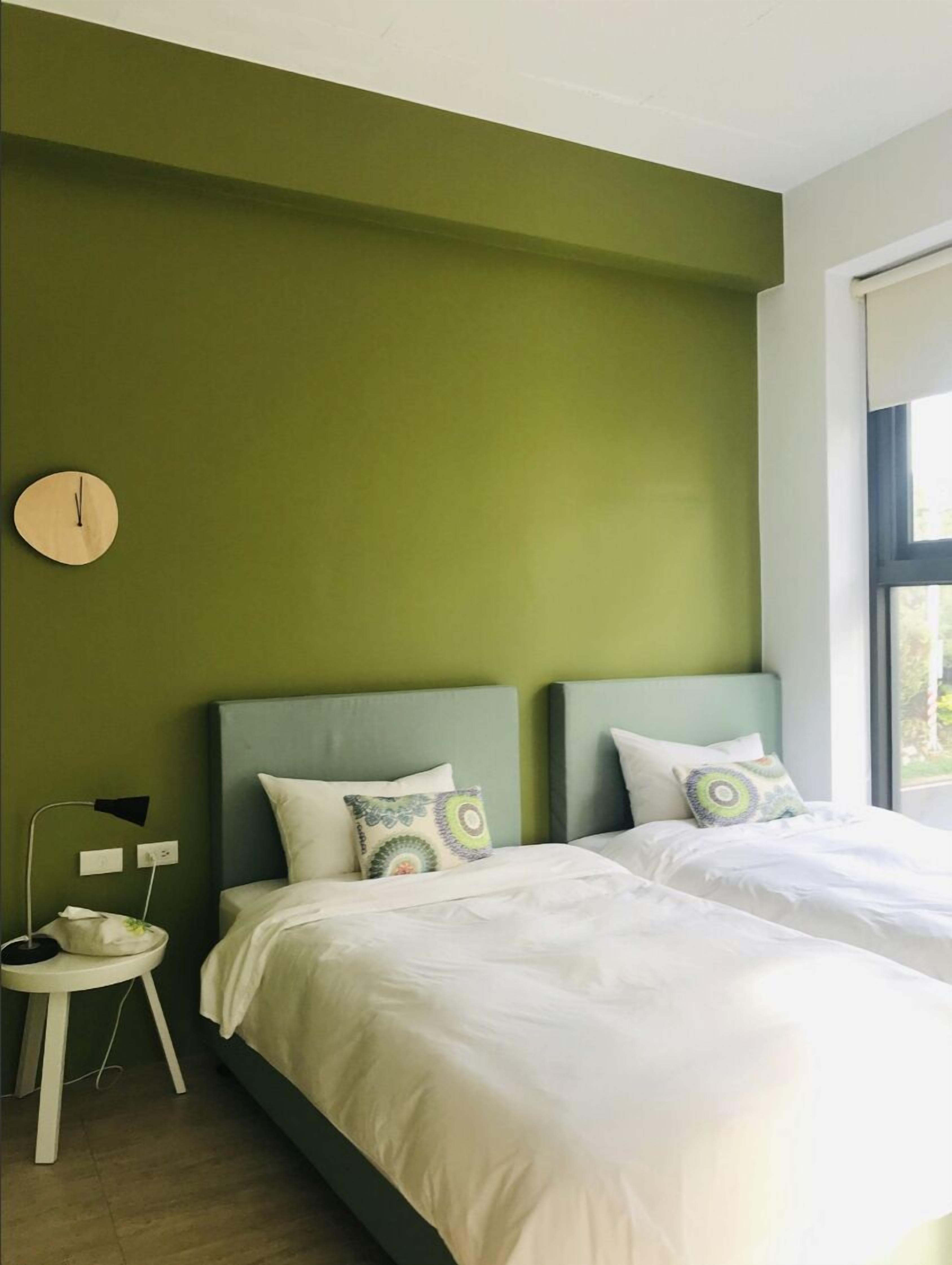 Un dormitorio con dos camas, paredes verdes, un reloj y una ventana.