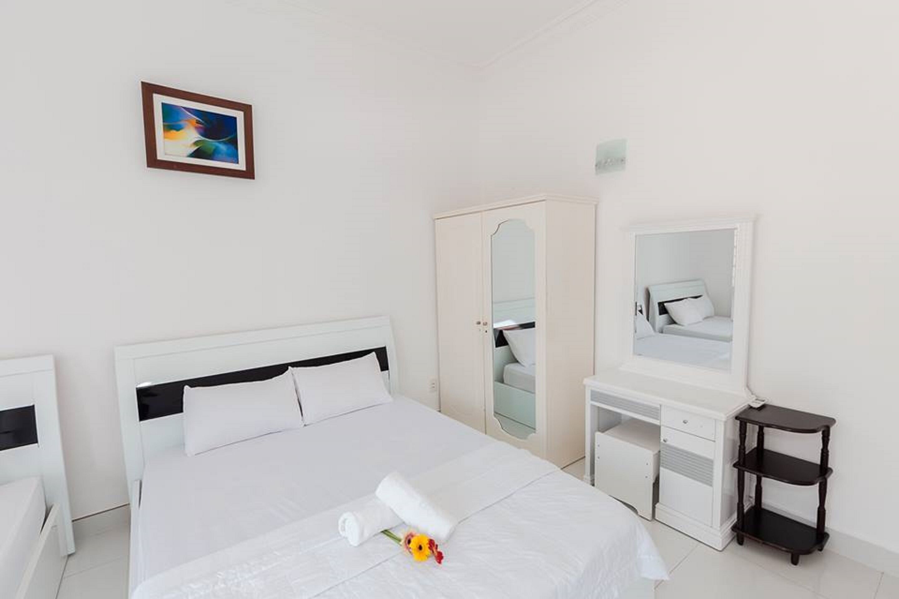 A hotel room with a bed, a desk, a wardrobe, a mirror, and a small table.