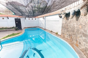 A swimming pool with a clear blue water surface, surrounded by a stone wall and a white fence.