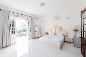 A spacious bedroom with a large bed, a dresser, a nightstand, and a door leading to a balcony.