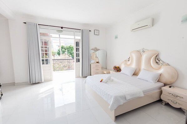 A spacious bedroom with a large bed, a nightstand, a dresser, and a view of the outdoors through a sliding glass door.