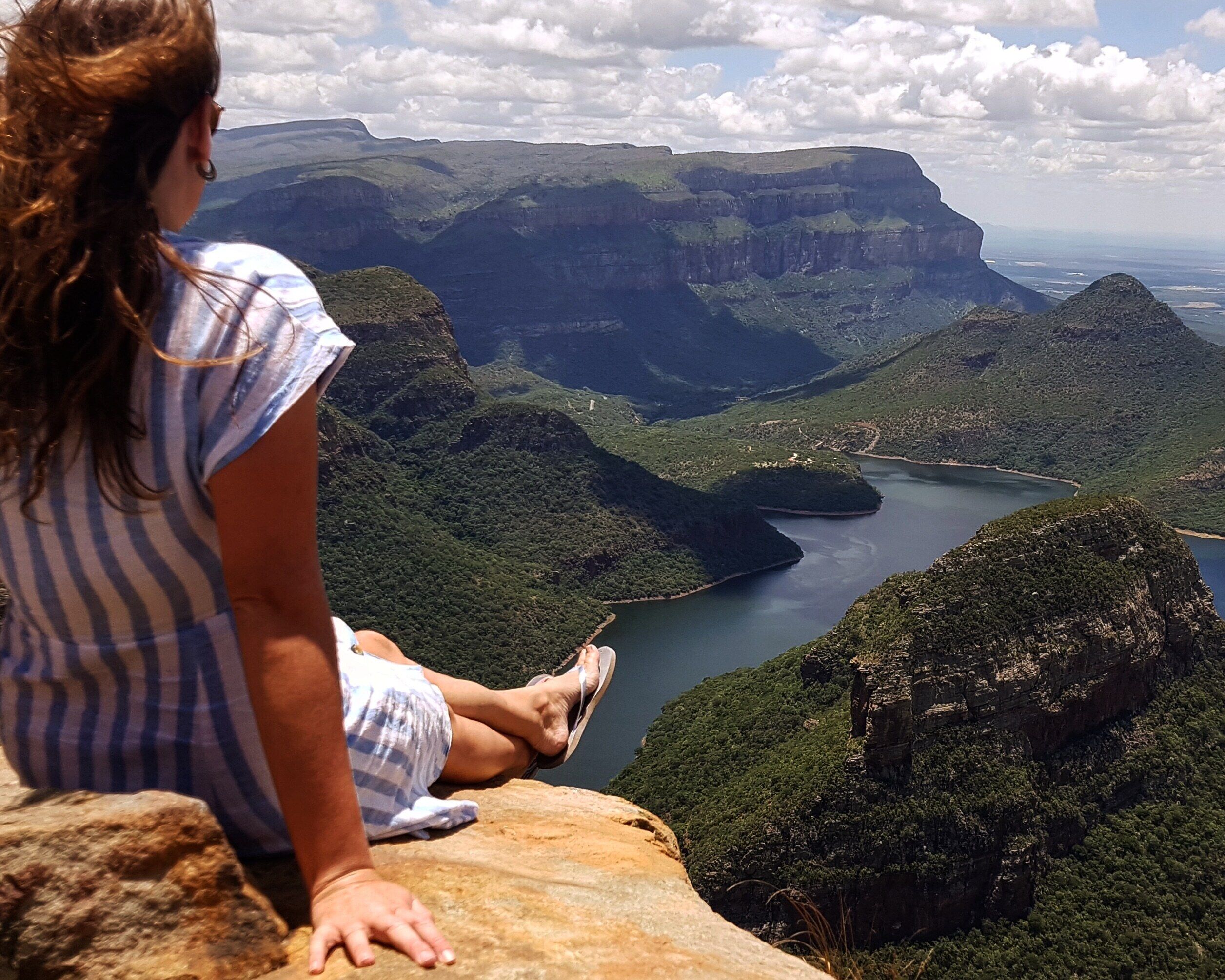 A person sitting on a rock overlooking a valley with a river and mountains.
