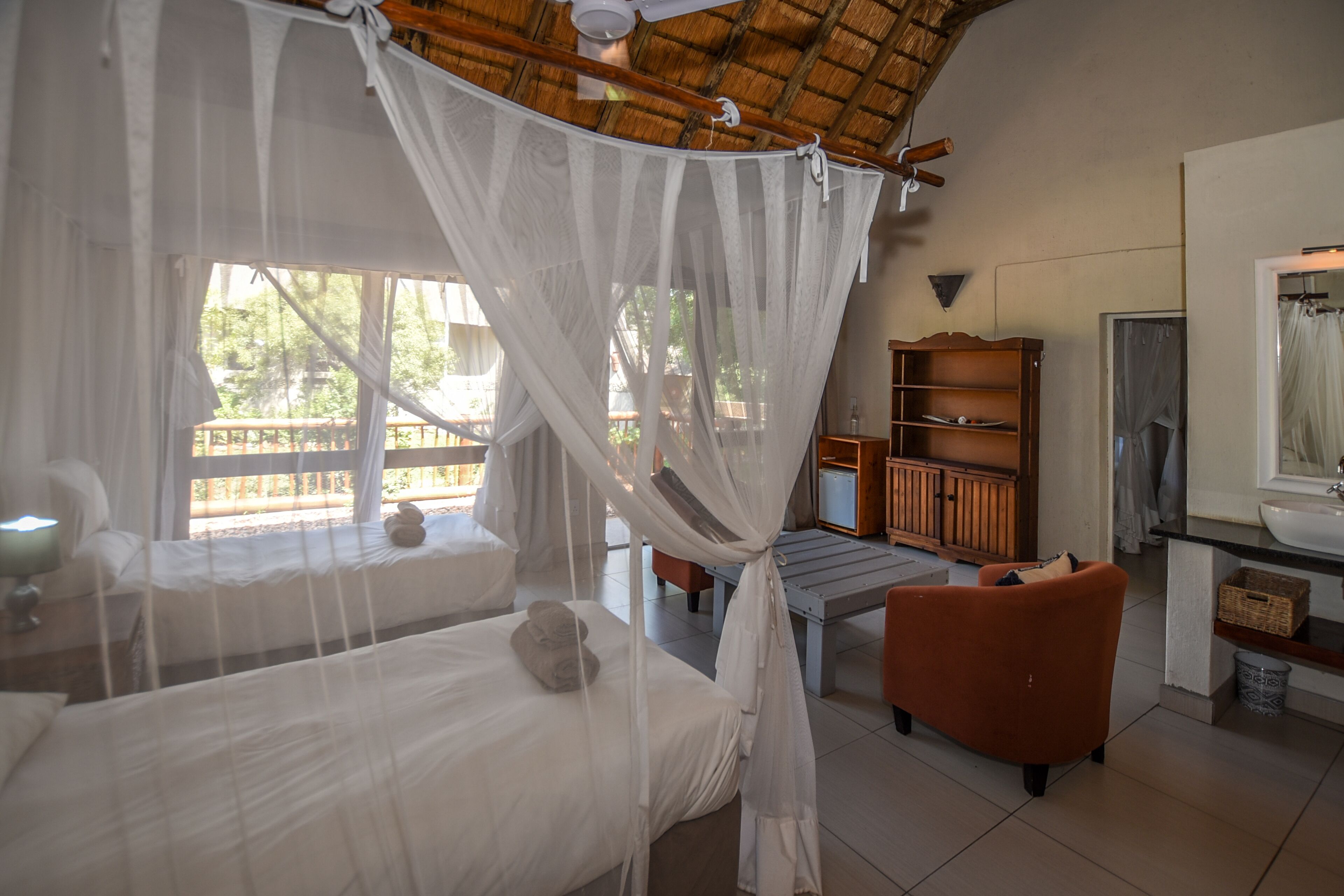 A room with a bed, a daybed, a wooden cabinet, and a window with a view of greenery.